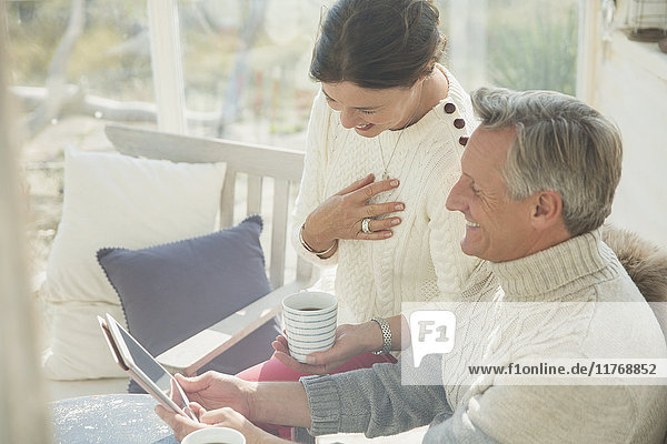 Ein reifes Paar trinkt Kaffee und benutzt ein digitales Tablett auf der Veranda.