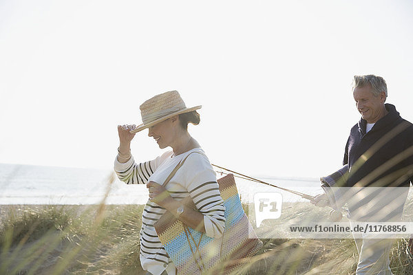 Mature couple with fishing rod walking in sunny summer beach grass