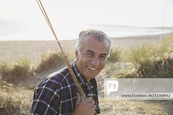 Portrait smiling senior man with fishing rod walking on sunny beach