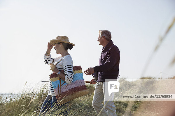 Erwachsenes Paar  das auf einem sonnigen Strandgrasweg spazieren geht.
