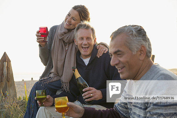 Verspielte reife Freunde trinken Champagner am Strand