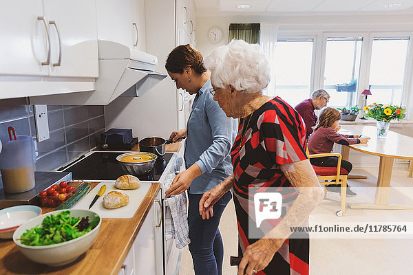 Side view of senior woman and daughter cooking food in kitchen