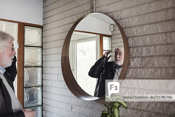 Älterer Mann schaut in den Spiegel  während er im Zimmer steht.