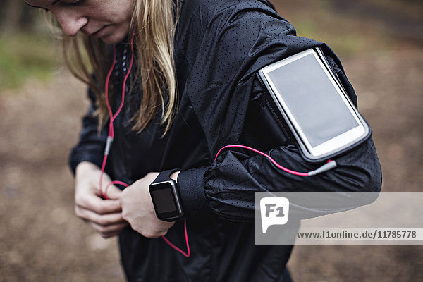 Midsection of female athlete with smart phone in arm band fixing headphones to jacket in forest