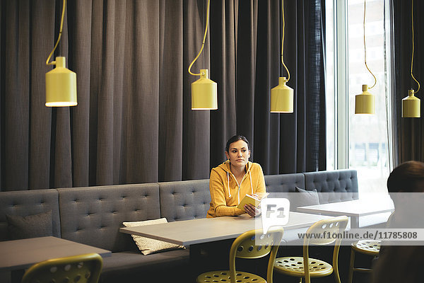 Mittlere erwachsene Geschäftsfrau mit Buch am Tisch in der Cafeteria im Büro