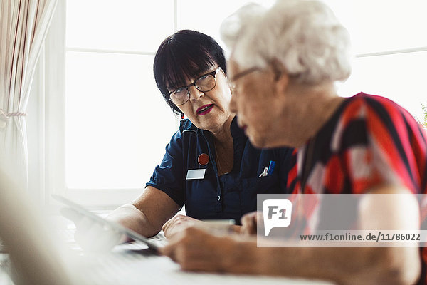 Caretaker assisting senior woman in using digital tablet at home
