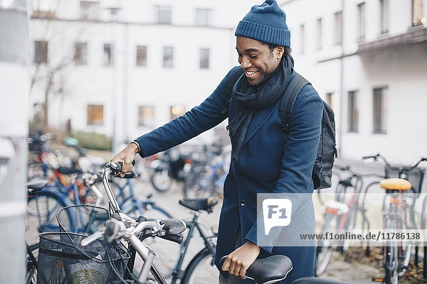 Fröhlicher junger männlicher Student steht mit dem Fahrrad in der Stadt