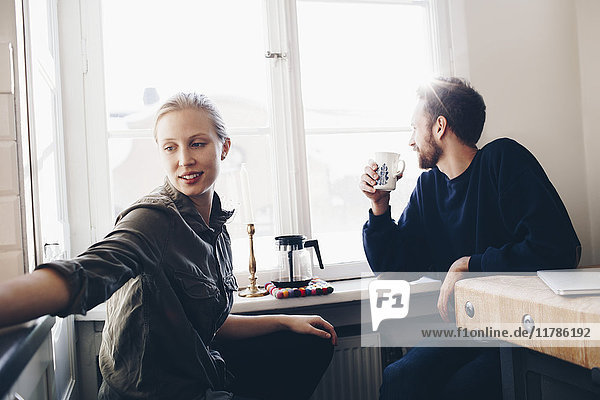 Paar sitzt in der Küche und trinkt zu Hause Kaffee am Fenster.
