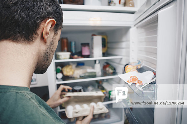 Mann mit Eierkarton am Kühlschrank in der Küche