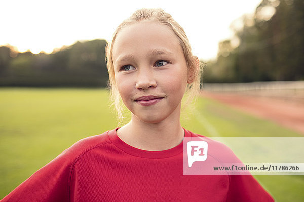 Girl wearing red t-shirt standing on soccer field against sky