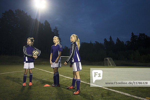 Mädchen  die in der Abenddämmerung auf dem Fußballplatz gegen den Himmel stehen.