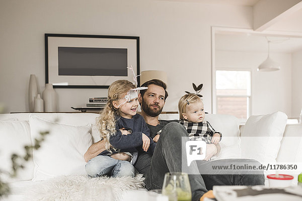 Mid adult man with daughters sitting on sofa in living room at home