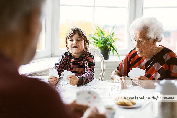 Glücklicher Junge beim Kartenspielen mit Urgroßeltern zu Hause