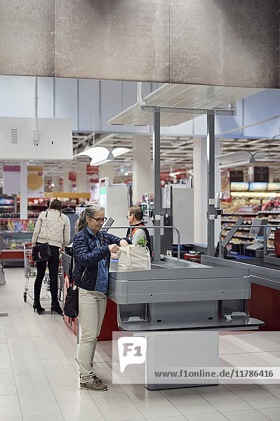 Reife Frau stehend mit Einkaufstasche an der Kasse im Supermarkt