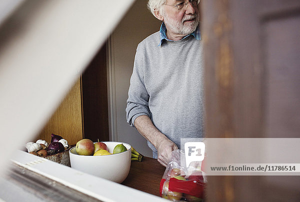 Senior Mann beim Entnehmen von Äpfeln aus der Packung,  während er an der Küchenzeile steht.