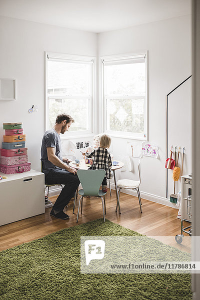 Father playing with daughter at small dining table in playroom