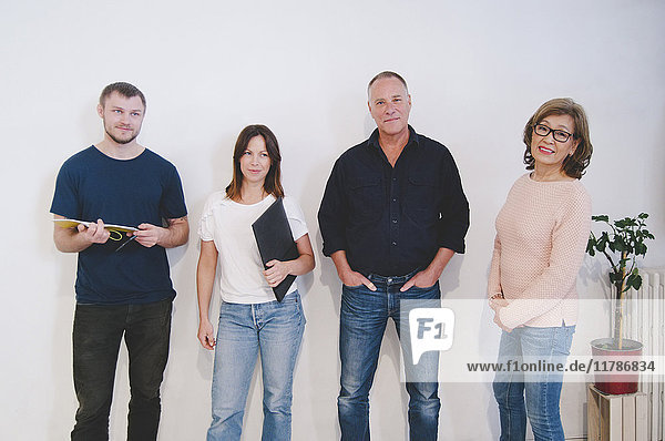 Portrait of confident creative business people standing against white wall in office