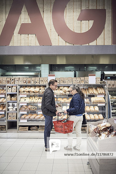 Erwachsenes Paar steht mit Korb gegen Brotgestell im Supermarkt