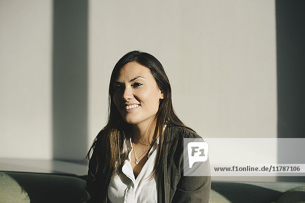 Nachdenkliche Geschäftsfrau lächelt  während sie in der hell erleuchteten Bürolobby sitzt.