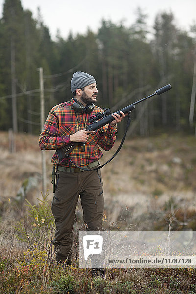 Männlicher Jäger schaut weg während er das Gewehr im Wald hält.