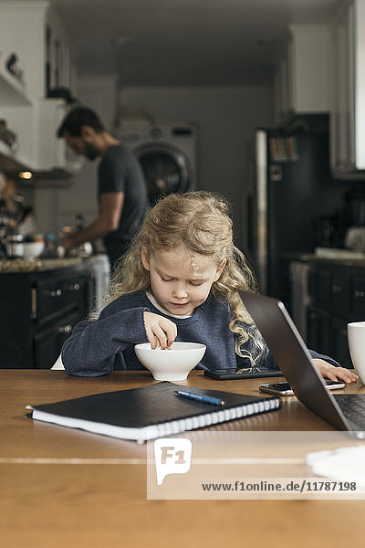 Girl having breakfast at table with father and sister in kitchen at home