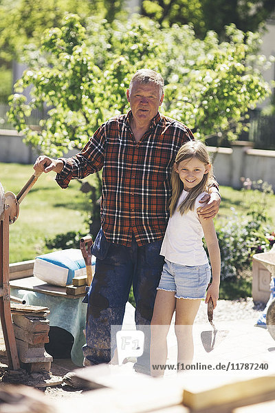 Portrait of grandfather and granddaughter standing by cement mixer in yard