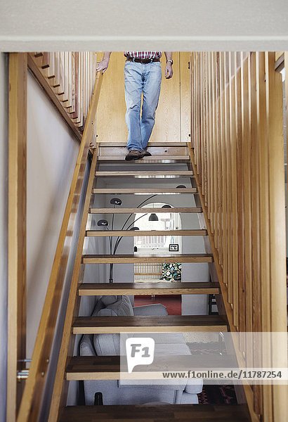 Niedriger Abschnitt des älteren Mannes  der zu Hause die Holztreppe hinuntergeht.