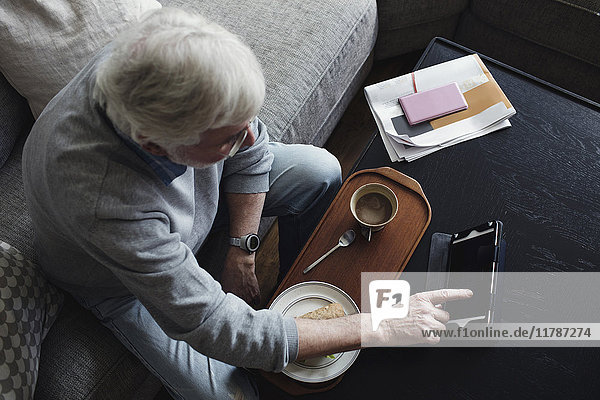 Hochwinkelansicht eines älteren Mannes mit digitalem Tablett während des Frühstücks zu Hause