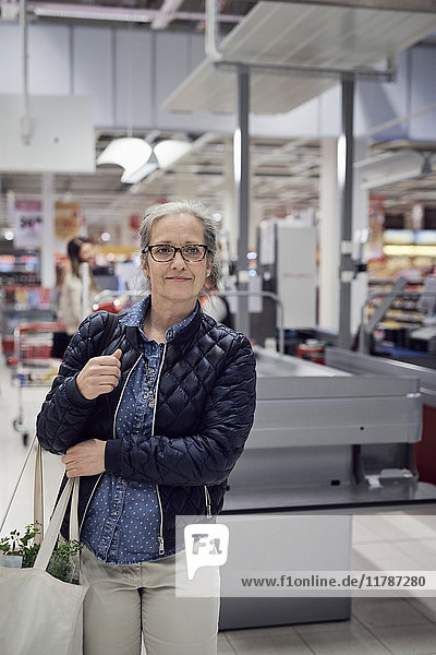 Smiling mature woman carrying shopping bag while looking away against checkout at supermarket