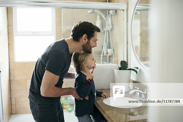 Seitenansicht des Vaters beim Zähneputzen der Tochter am Waschbecken im Bad