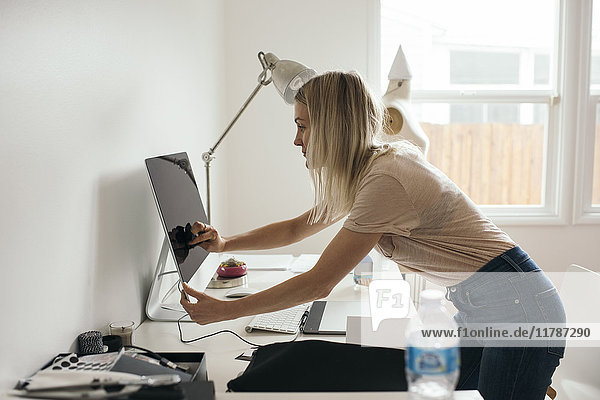 Side view of female graphic designer touching desktop monitor at home