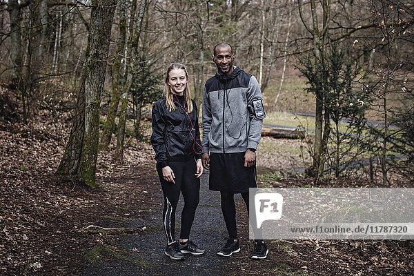 Full length portrait of confident male and female athletes standing in forest