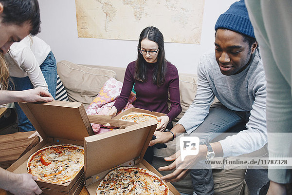 Hochwinkelansicht von jungen Freunden beim Öffnen von Pizzakartons im Schlafsaal