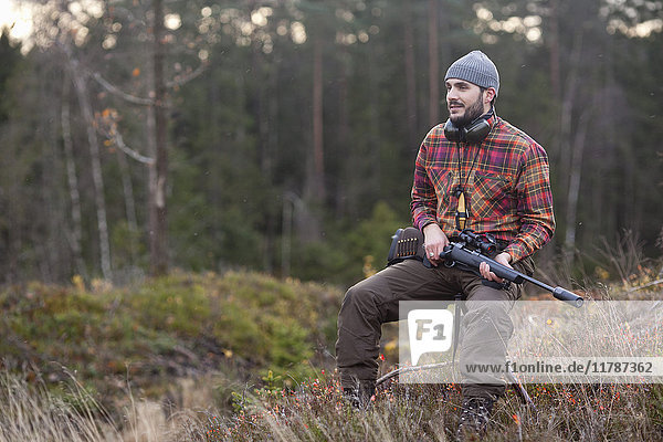 Nachdenklicher männlicher Jäger der auf einem Hocker im Wald sitzt.