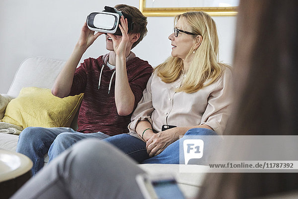 Mutter  die den Sohn mit einem Virtual-Reality-Headset anschaut  während sie auf dem Sofa sitzt.