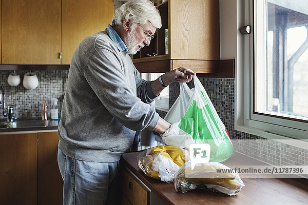 Senior Mann  der Pakete aus der Plastiktüte am Küchentisch entnimmt