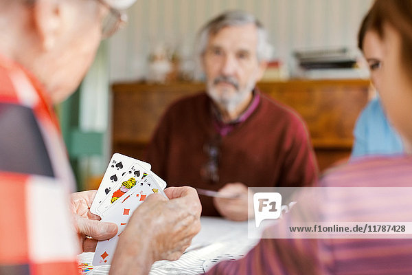 Abgeschnittenes Bild einer älteren Frau  die mit ihrer Familie zu Hause Karten spielt.
