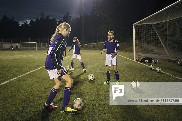 Mädchen üben mit Fußbällen per Torpfosten auf dem Spielfeld nachts