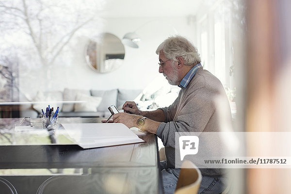 Seitenansicht eines älteren Mannes  der ein digitales Tablett benutzt  während er den Papierkram durch Glas betrachtet.