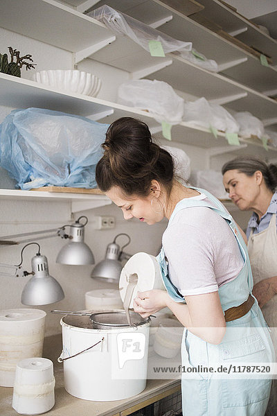 Senior Töpferin beim Anblick einer jungen Mitarbeiterin  die in der Werkstatt Ton aus der Vase in den Eimer gießt.