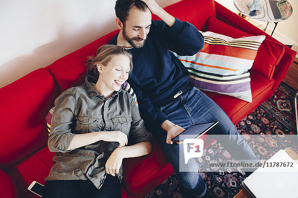 High angle view of couple looking at digital tablet while relaxing on sofa in living room
