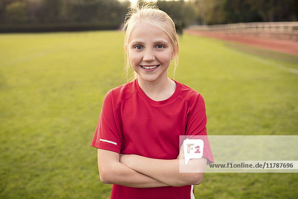 Portrait eines glücklichen Mädchens im roten T-Shirt stehend mit gekreuzten Armen auf dem Fußballfeld