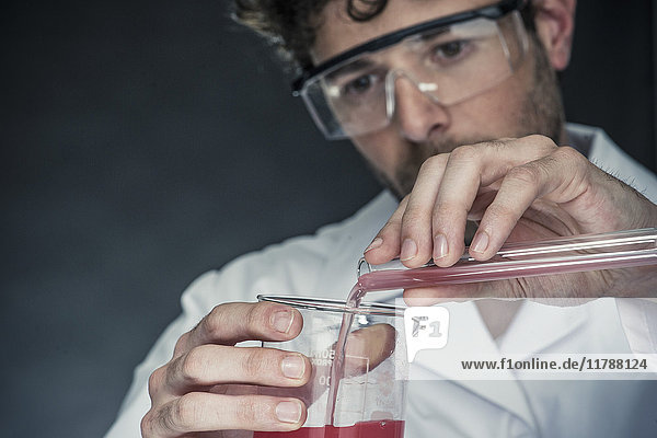 Wissenschaftler gießt Flüssigkeit aus dem Reagenzglas in ein Becherglas