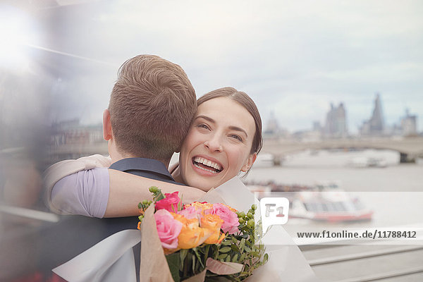 Glückliche  dankbare Frau erhält Blumenstrauß  umarmt Freund am städtischen Ufer