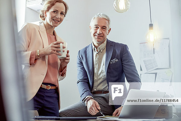 Portrait lächelnde  selbstbewusste Geschäftsleute beim Kaffeetrinken und Arbeiten am Laptop im Büro