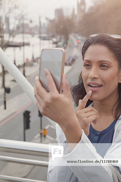 Woman checking makeup with camera phone on urban bridge  London  UK