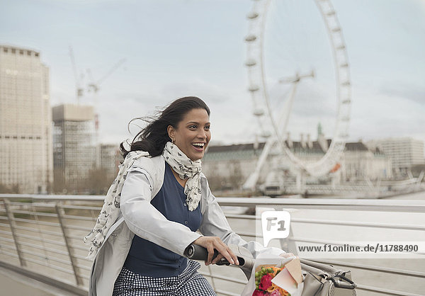 Enthusiastic  smiling woman bike riding on bridge near Millennium Wheel  London  UK