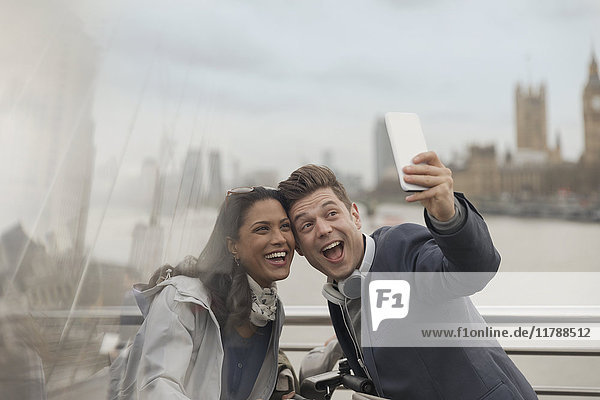 Playful couple tourists taking selfie with camera phone on bridge  London  UK