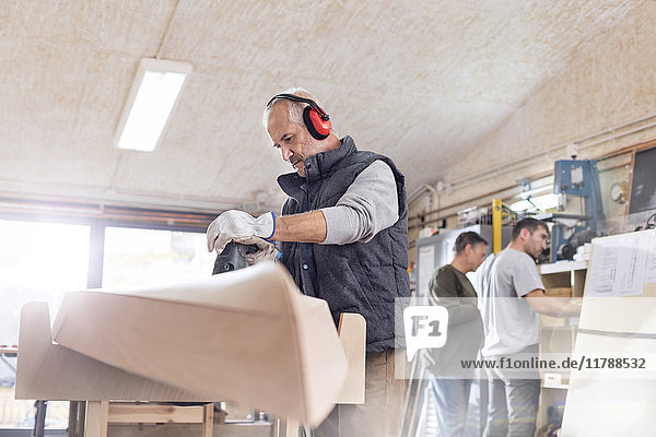 Senior Schreiner mit Schleifmaschine  Schleifen von Holzbooten in der Werkstatt