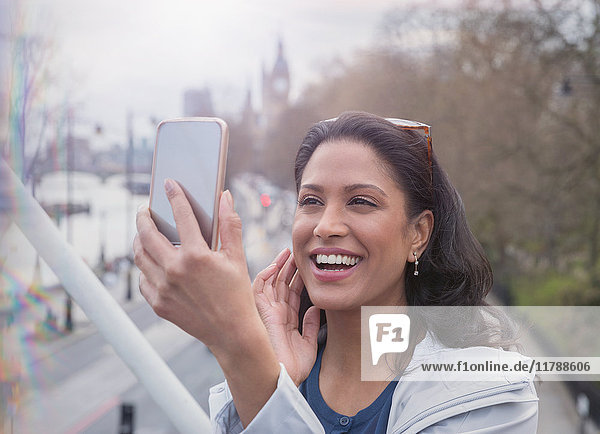 Smiling  confident woman taking selfie with camera phone on urban bridge